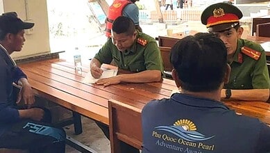 Police officers in uniform talking with civilians at a wooden table indoors.
