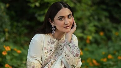 Yumna Zaidi in traditional attire, smiling outdoors with greenery in the background.