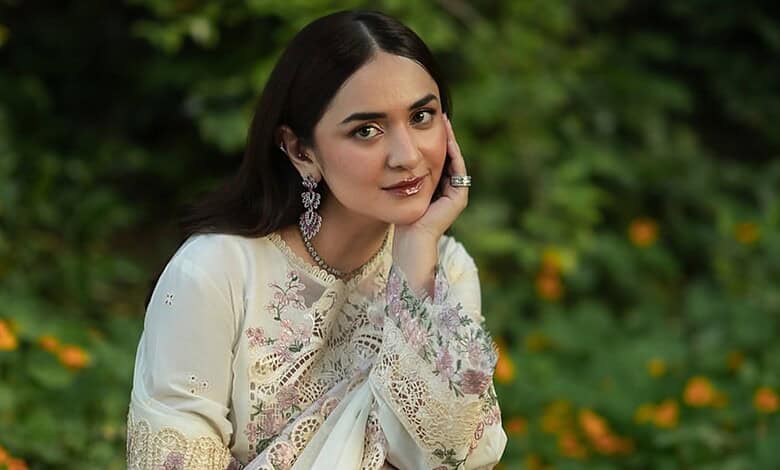 Yumna Zaidi in traditional attire, smiling outdoors with greenery in the background.