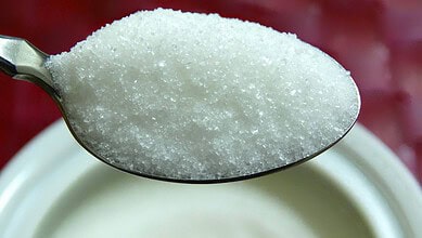 Close-up of a spoonful of raw sugar crystals over a sugar bowl.