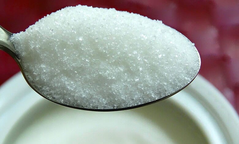Close-up of a spoonful of raw sugar crystals over a sugar bowl.