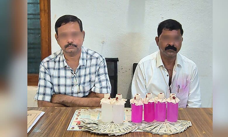 Two men seated at a table with pink bottles, cash, and a cake, in an indoor setting.