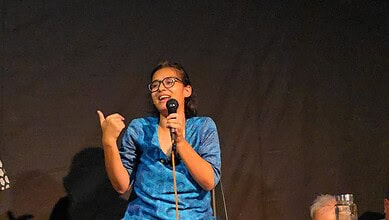 Neha Bora speaking passionately at a public event with a microphone in hand.