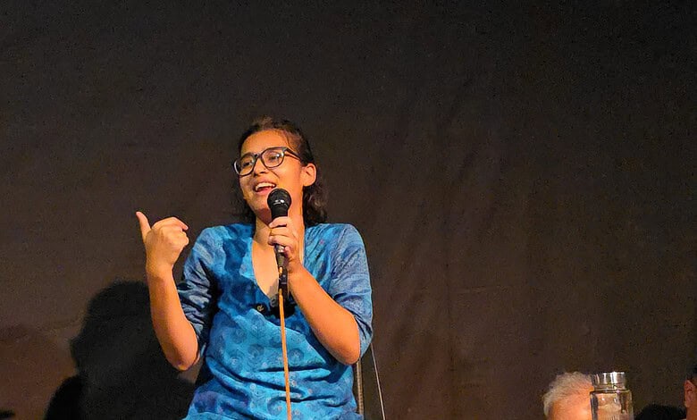 Neha Bora speaking passionately at a public event with a microphone in hand.