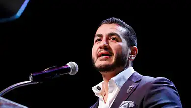 Abdul El-Sayed delivering speech at a public event in a suit and white shirt.