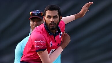 Cricketer in pink jersey preparing to bowl during a match.