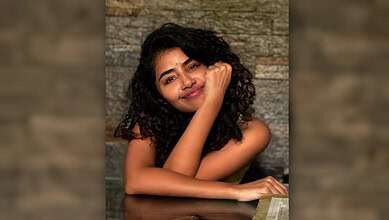 Young woman with curly hair smiling and resting her chin on her hand.