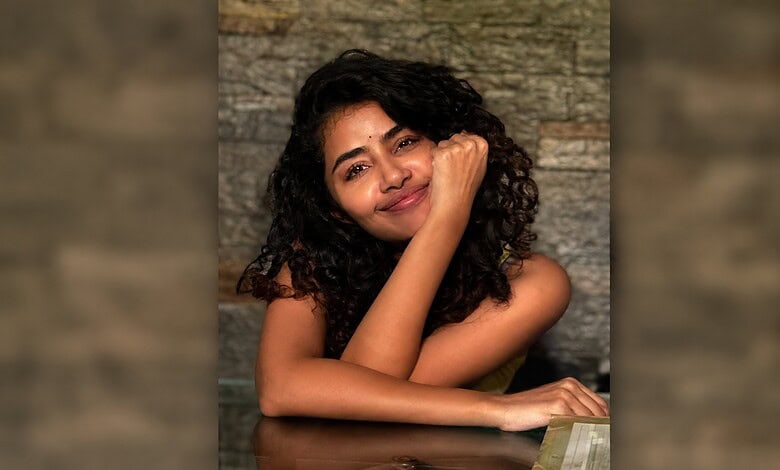 Young woman with curly hair smiling and resting her chin on her hand.
