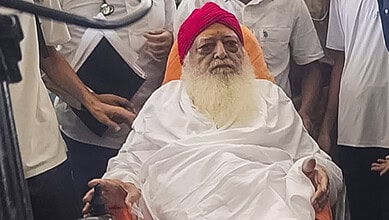 Asaram Bapu seated with a pink turban and white robes, surrounded by supporters.