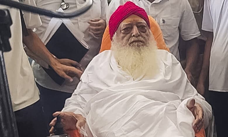 Asaram Bapu seated with a pink turban and white robes, surrounded by supporters.