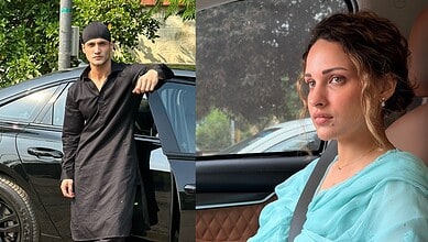 Young man in black traditional attire leaning on a car outside.