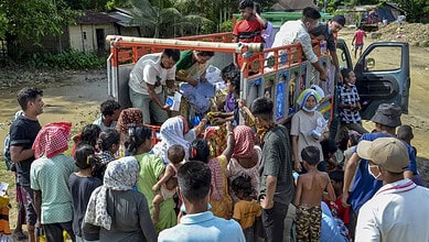 Flood-affected people being evacuated in Assam with rescue workers and a truck.