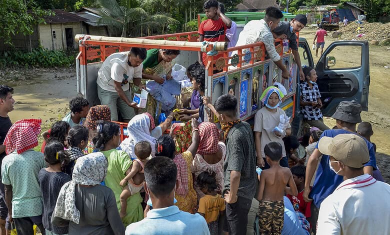 Flood-affected people being evacuated in Assam with rescue workers and a truck.