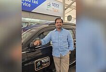 Man standing next to a Bharat Taxi vehicle at a transportation hub in Telangana.