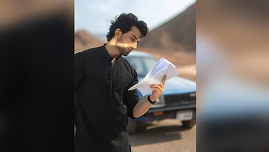 Pak actor Bilal Abbas Khan reading a script outdoors with mountains in the background.