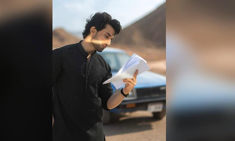 Pak actor Bilal Abbas Khan reading a script outdoors with mountains in the background.
