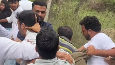 Group of men engaged in a physical altercation outdoors near a wire fence.