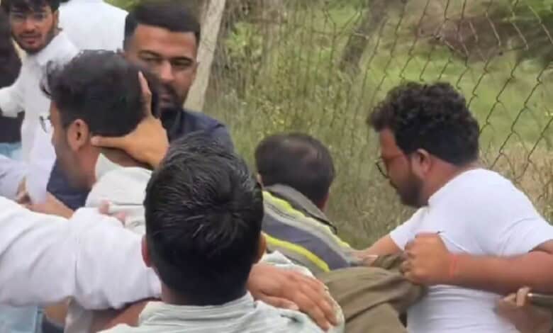 Group of men engaged in a physical altercation outdoors near a wire fence.