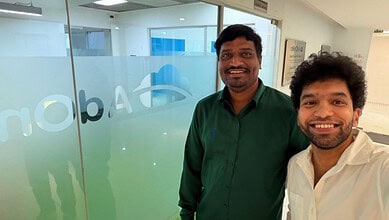 Two men smiling inside an office, one in a green shirt and the other in a white shirt.