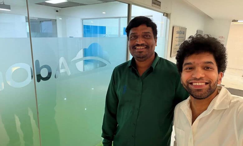 Two men smiling inside an office, one in a green shirt and the other in a white shirt.