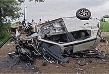 Upside-down car crash scene with debris and onlookers in the background.