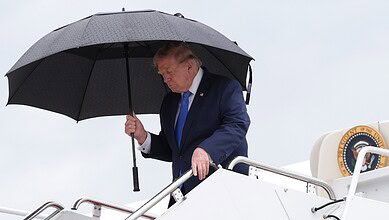 Donald Trump holding an umbrella while on a plane, looking downwards.