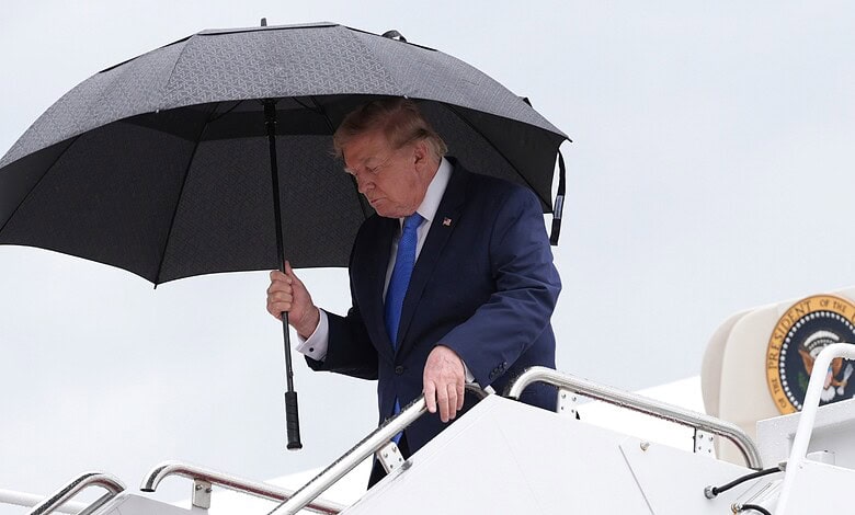 Donald Trump holding an umbrella while on a plane, looking downwards.