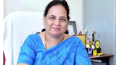 Waheeda Sultana in a blue saree smiling at her desk in an office setting.