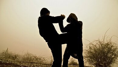 Two silhouetted figures fighting outdoors at sunset or sunrise.