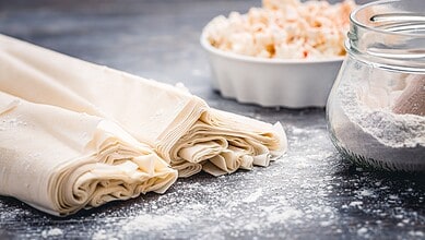 Rolled pastry dough with flour and baking ingredients on a rustic surface.