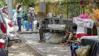 Street vendor sitting on footpath with cart and goods in an urban area.