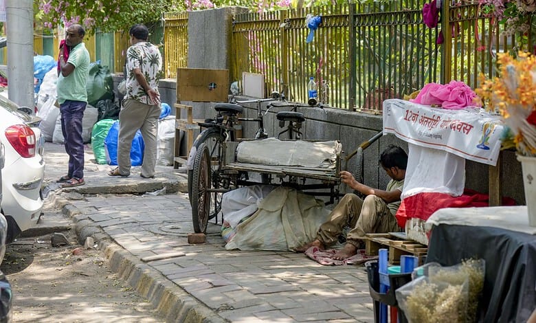 Street vendor sitting on footpath with cart and goods in an urban area.