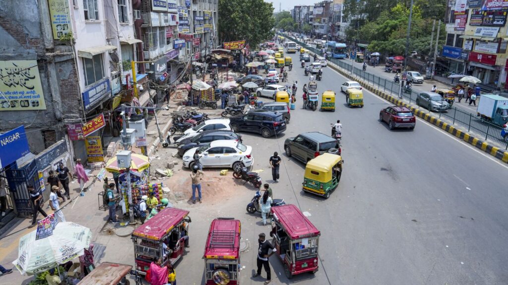 Busy street scene with parked vehicles, pedestrians, and street vendors in an urban area.
