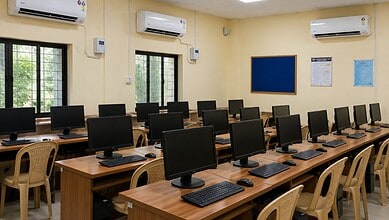 Computer lab with multiple desktops and chairs in a well-lit room.