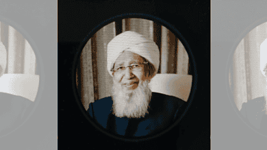 Grand Mufti with white beard and turban, smiling, seen through a circular mirror.