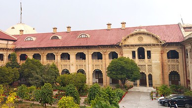 Historic building with ornate architecture and lush greenery in front, under a clear sky.
