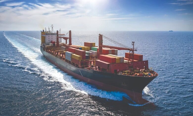 Large cargo ship sailing through open sea with containers onboard and a clear sky.
