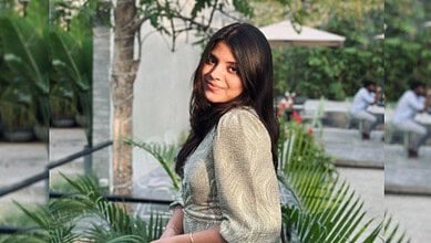 Young woman with long dark hair smiling outdoors in a garden setting.