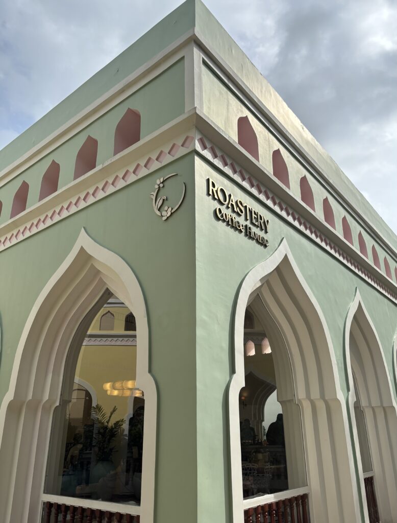 Exterior of Roastery Coffee Shop with arched windows and pastel green walls.