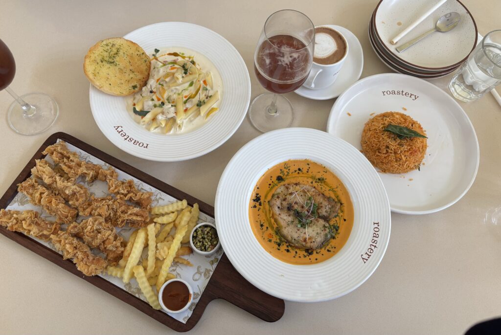 Variety of dishes including fried chicken, pasta, and a croquette with drinks on a table.