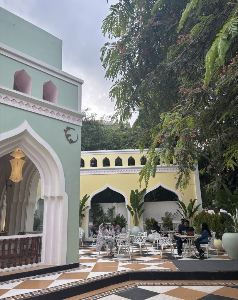 People sitting at tables in an outdoor courtyard with Islamic architectural elements and lush greenery.
