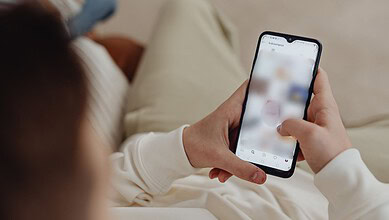 Person using a smartphone while sitting on a sofa, browsing content.
