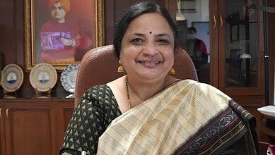 JNU Vice-Chancellor smiling in office, wearing traditional saree and gold jewellery.