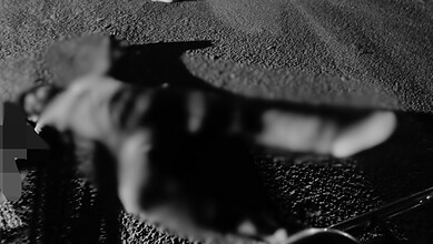 A blurred image of a person lying on the ground at night with a vehicle nearby.