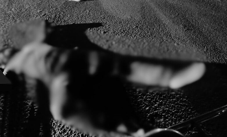 A blurred image of a person lying on the ground at night with a vehicle nearby.