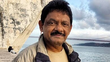 Shakeel Noorani, filmmaker, near a bridge with water in the background, during daytime.