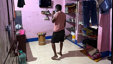 Man standing in a small room with pink walls, shelves, and hanging clothes.