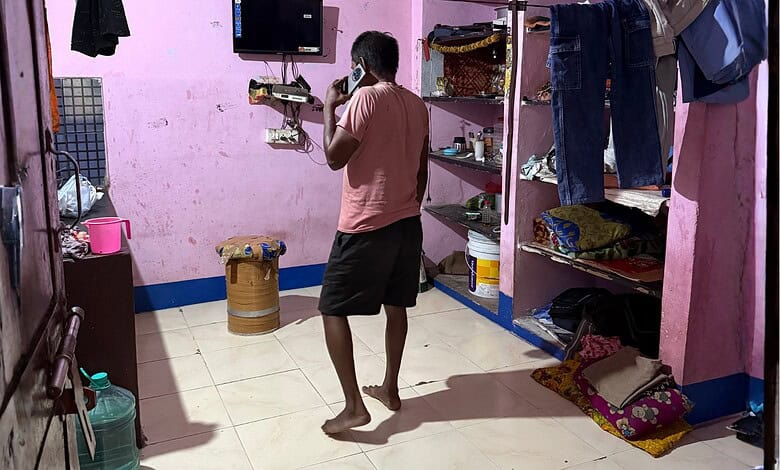 Man standing in a small room with pink walls, shelves, and hanging clothes.