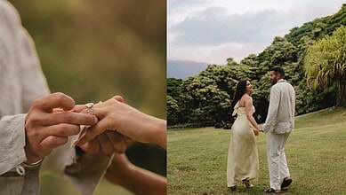 Couple getting engaged outdoors with lush green trees and cloudy sky in the background.