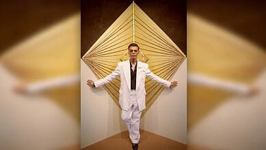 Celebrity posing in white suit against geometric background for Koffee With Karan season 9.